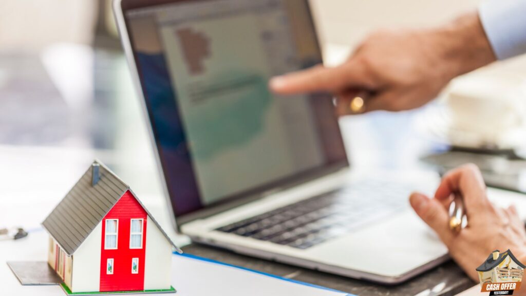 Two people using a laptop, with one person pointing at the screen, and a miniature house beside the laptop - We Buy Houses in Colleyville TX